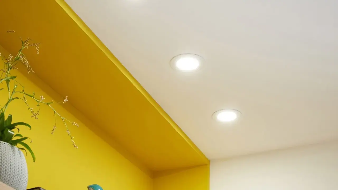 Trois spots lumineux éclairent un plafond blanc au-dessus d'une étagère jaune vif.