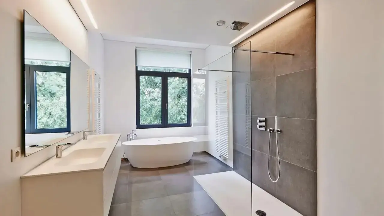 Salle de bain moderne avec baignoire îlot, double vasque et douche à l'italienne. L'éclairage intégré en hauteur applique une ambiance douce.