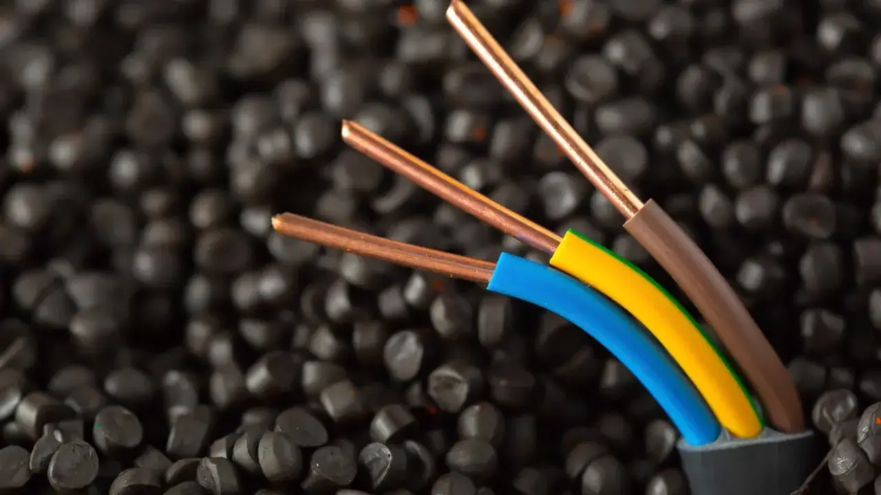 Trois fils électriques aux conducteurs en cuivre, dont un fil marron électrique, sortent d'un câble noir sur un fond de granulés noirs.
