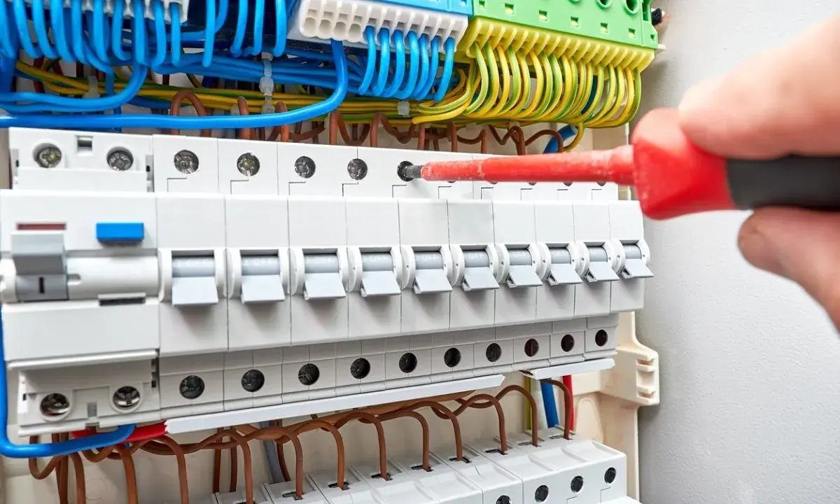 Main électrique avec disjoncteurs. Un tournevis rouge est utilisé pour ajuster une connexion, aidant à comprendre comment savoir quel fusible changer.