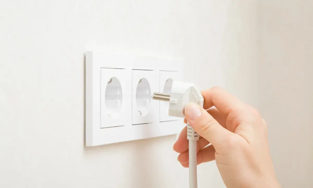 Main d'une personne branchant une prise électrique dans une prise murale triple.