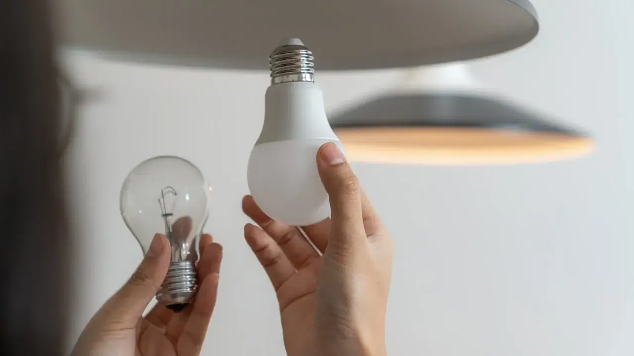 Une ampoule sans électricité, une ampoule LED moderne et une main tenant les deux, prête à remplacer l'ancienne.