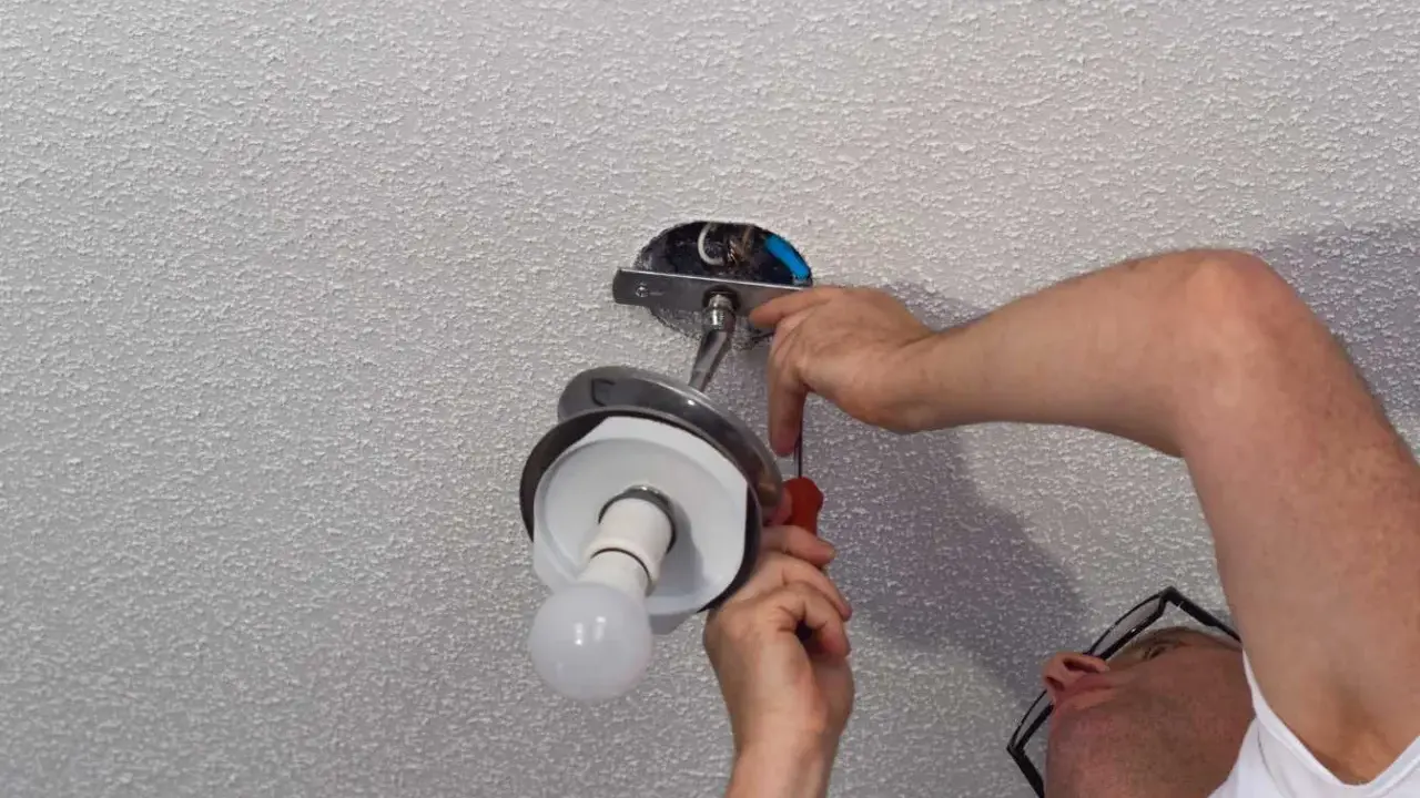 Un homme installe un luminaire au plafond avec un tournevis.