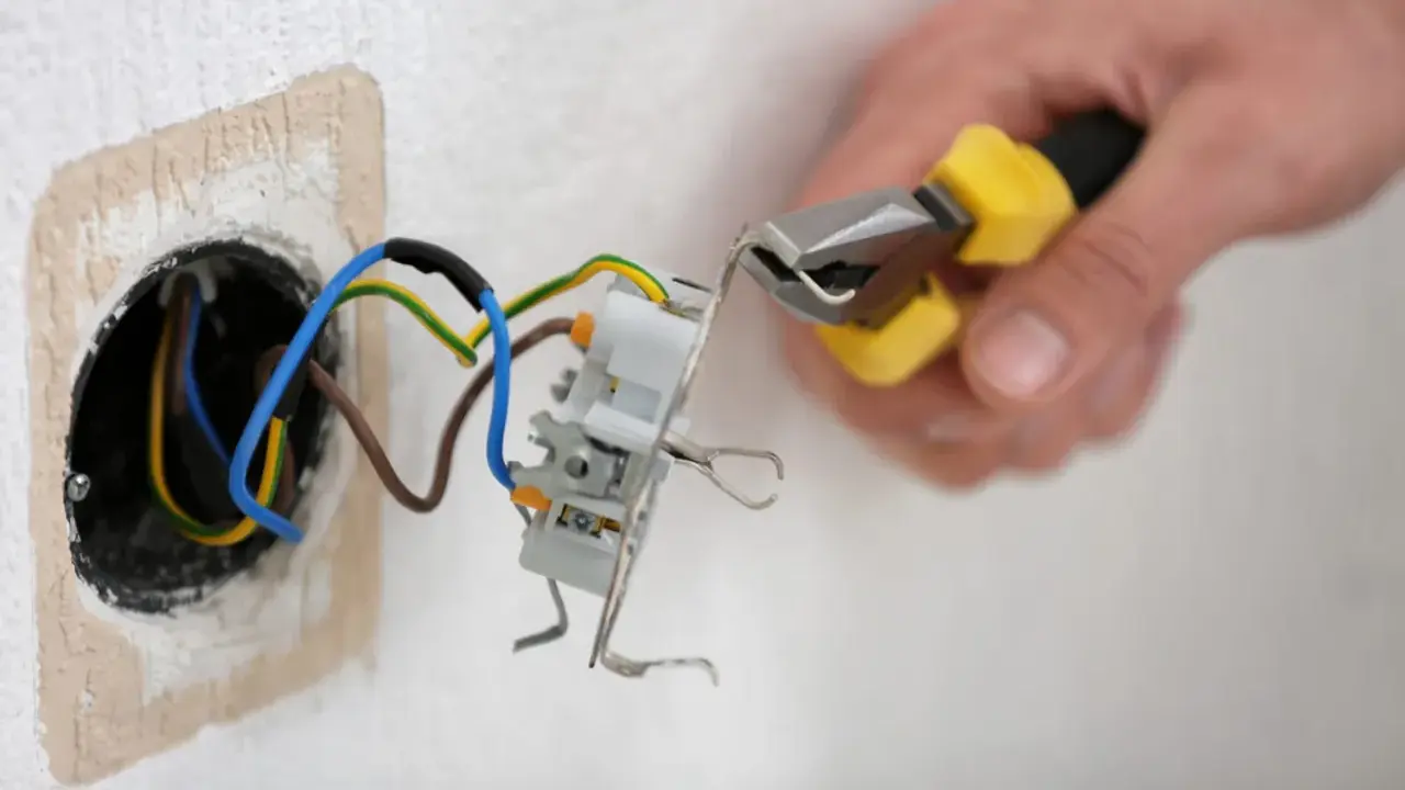 Mainteneur ajustant un fil bleu et marron dans une prise électrique.