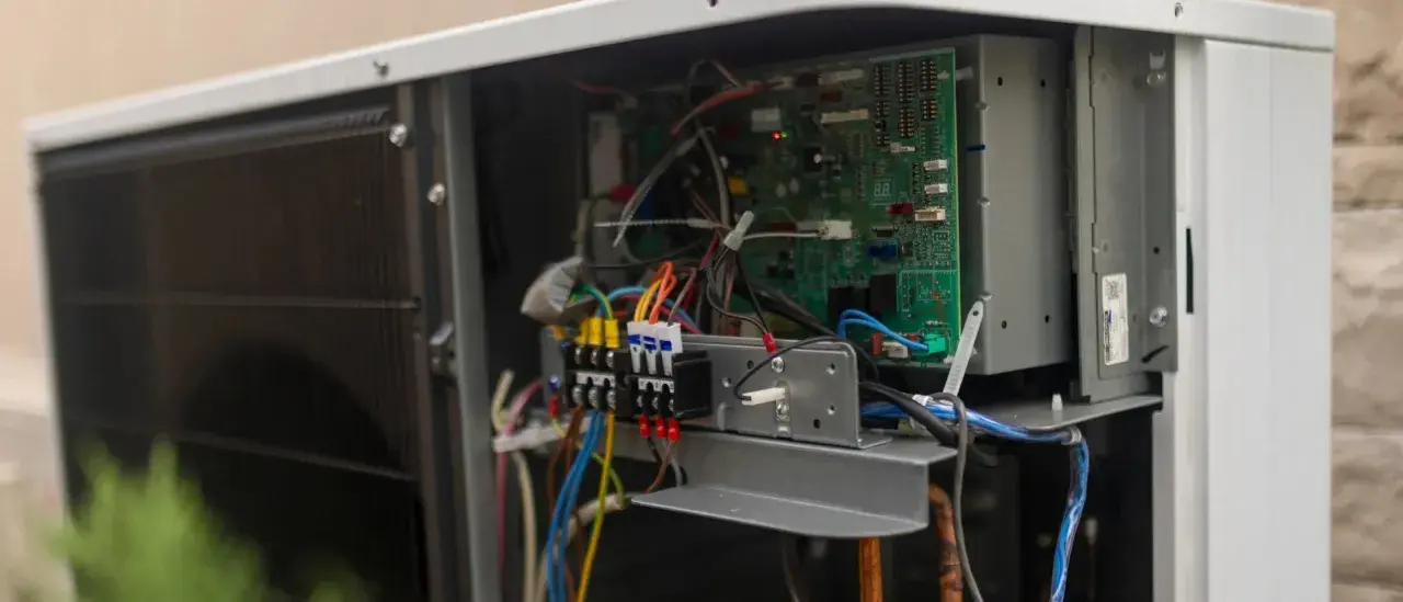Vue rapprochée des composants internes d'une pompe à chaleur, incluant la carte électronique et le disjoncteur.