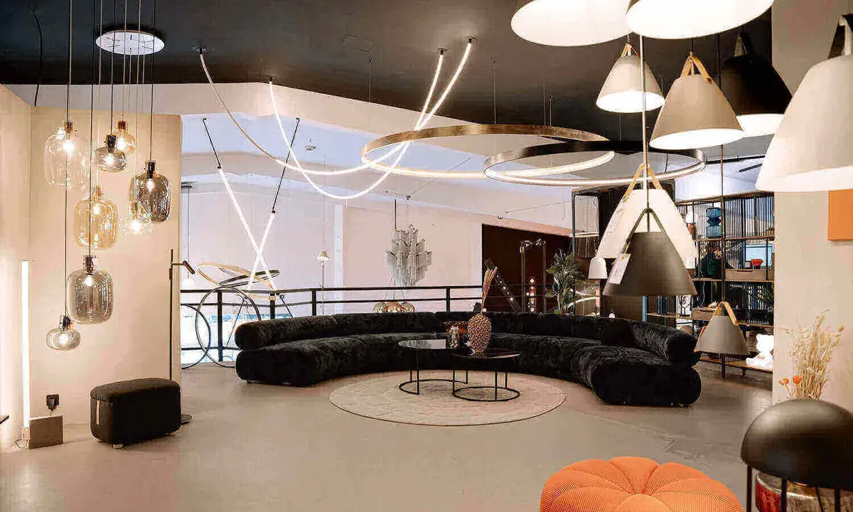 Un salon moderne avec un canapé incurvé noir, des tables basses, un tapis rond et une variété d'ampoules design suspendues au plafond.