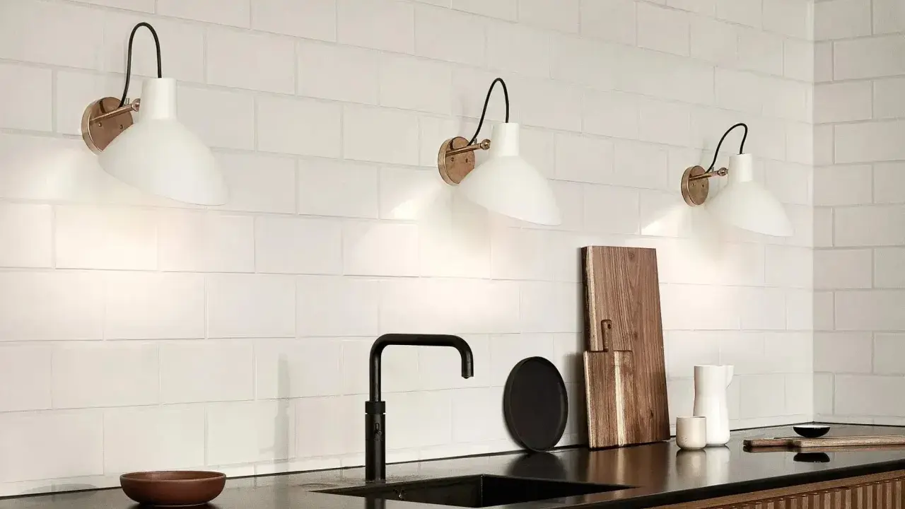 Trois appliques murales blanches avec un bras noir et une base dorée, éclairant un mur de carreaux blancs. Le branchement applique murale avec interrupteur est discret.