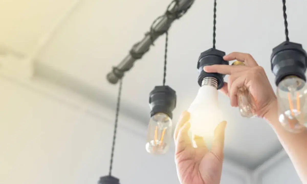 Main d'une personne installant une ampoule gradable dans un lustre.