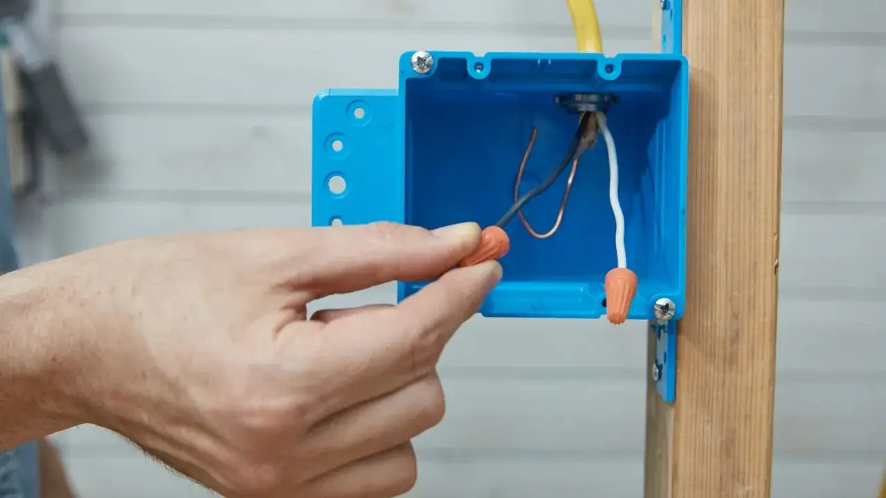Main tenant utilise un connecteur pour condamner une prise électrique. Les fils électriques sont visibles dans la boîte bleue.