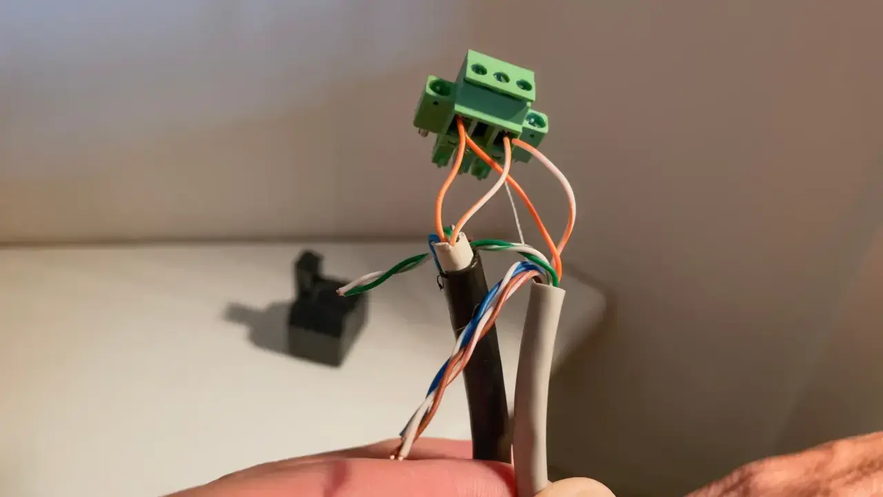 Connexion de fils électriques colorés à un connecteur vert. Un petit point lumineux attire l'œil sur le fil blanc.