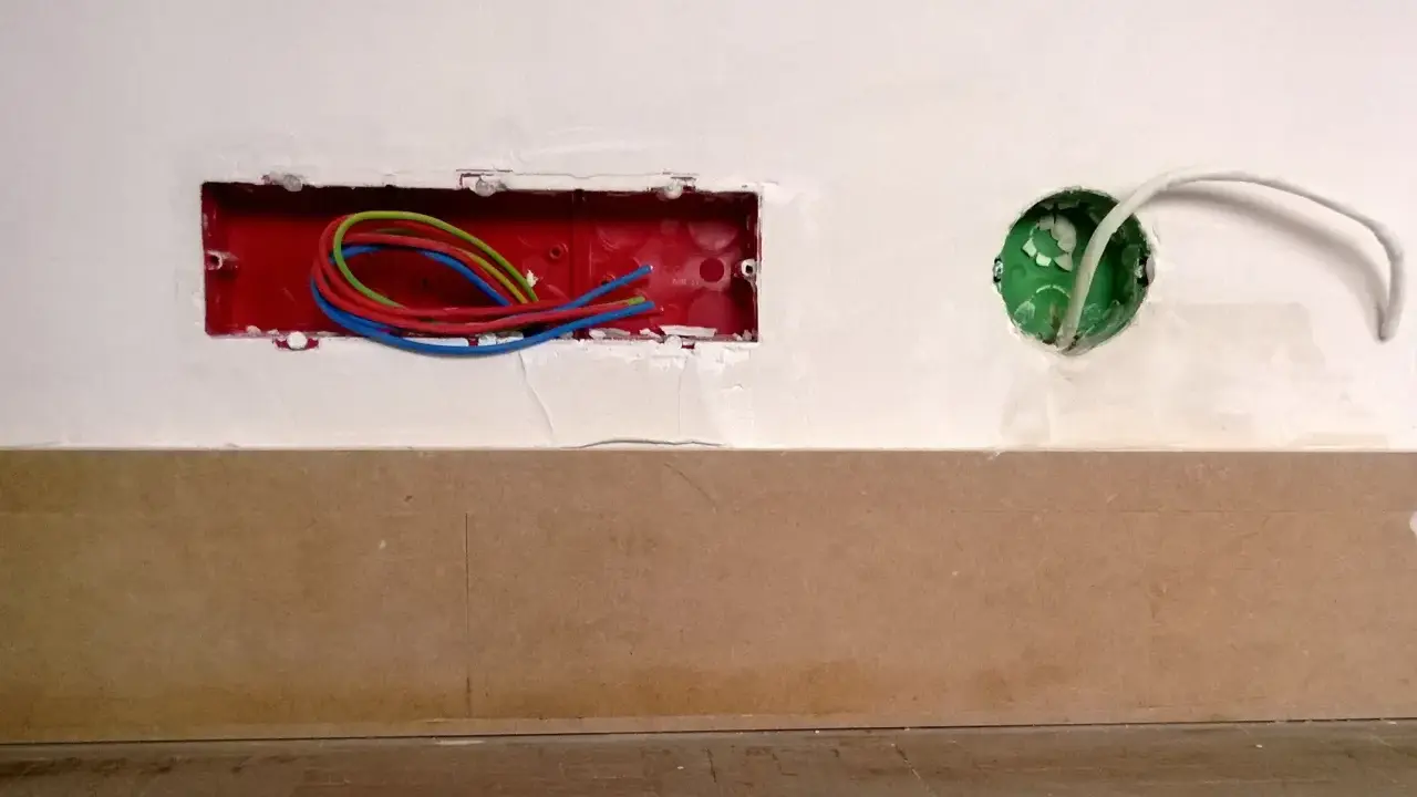 Boîtier rouge avec fils électriques colorés, prêt pour un interrupteur compteur électrique. Une boîte verte avec un câble blanc est visible à droite.