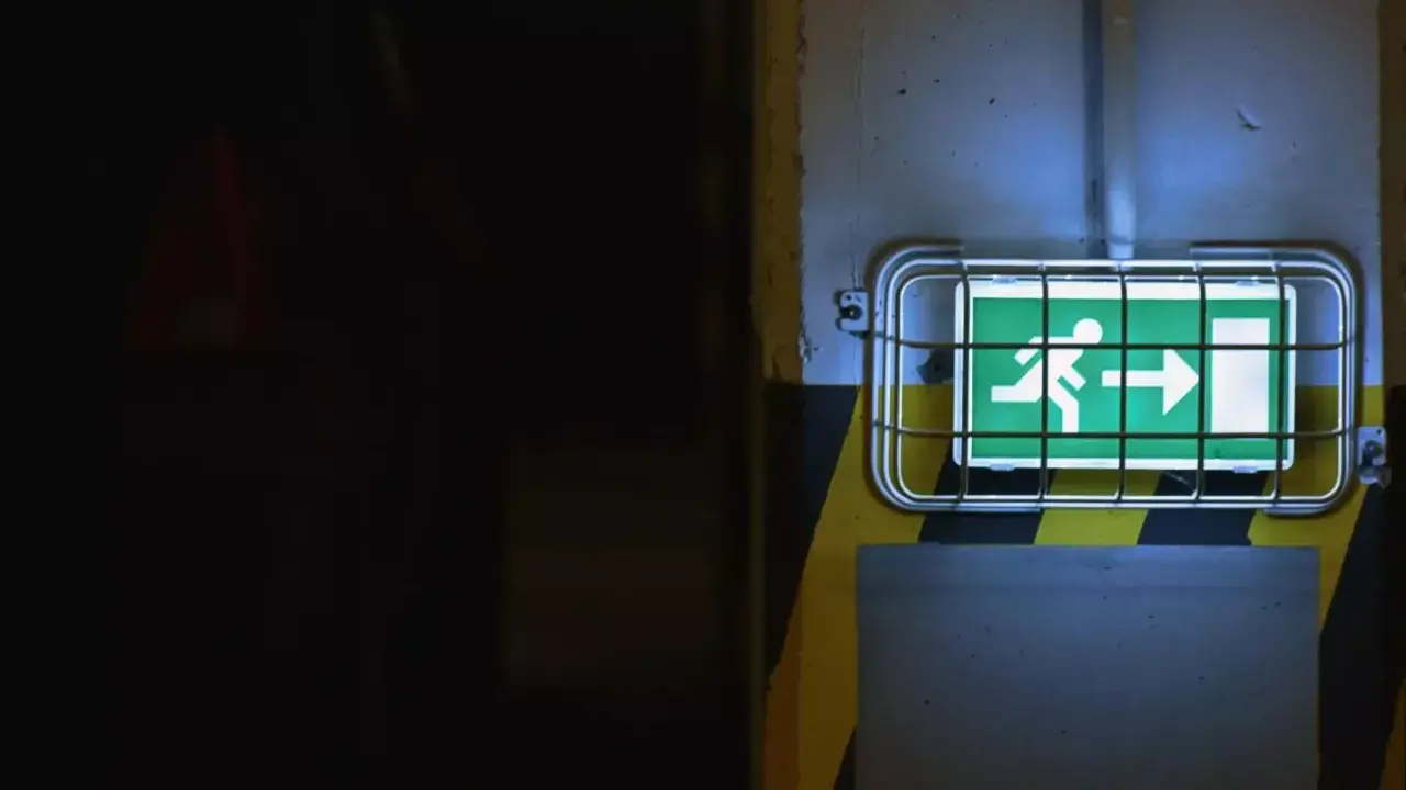 Panneau de sortie de secours vert lumineux, indiquant la direction à suivre. Le **baes signification** est claire : sécurité et évacuation.