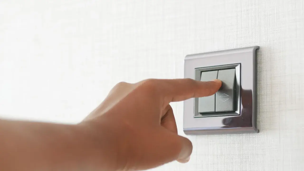 Doigt appuyant sur un interrupteur va et vient ou poussoir, sur un mur texturé.