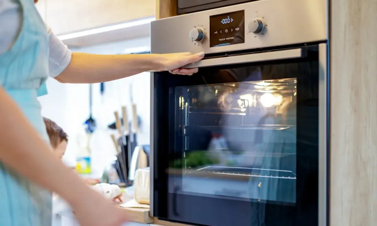 Une main ouvre la porte d'un four moderne. L'ampérage du four est réglé pour une cuisson parfaite.
