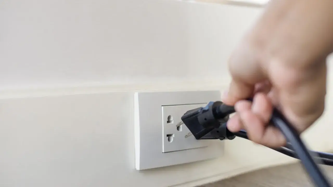 Main d'une personne branchant un appareil sur une prise murale. Une solution simple pour installer une prise électrique sans percer.