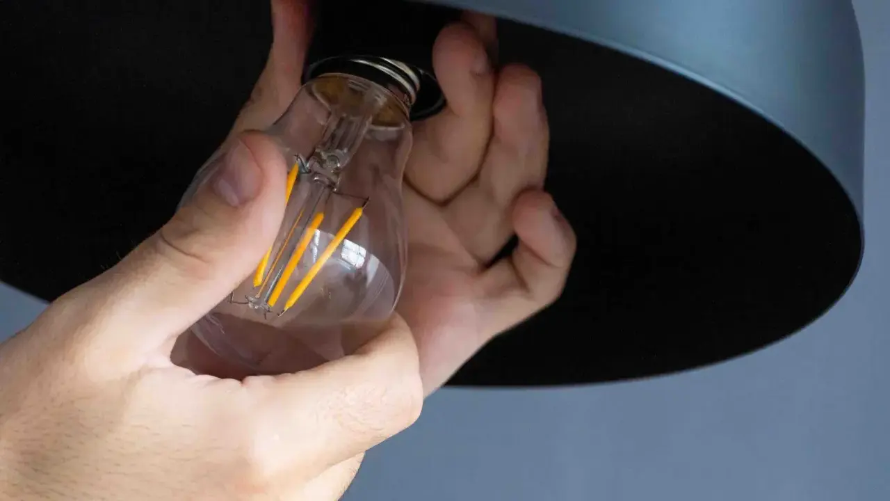Mains tenant une ampoule LED à filament, prête à être installée. La chaleur de l'ampoule est symbolisée par ses filaments jaunes lumineux.