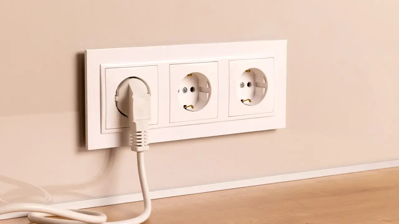 Prise électrique blanche avec un câble branché, installée à la hauteur du plan de travail.