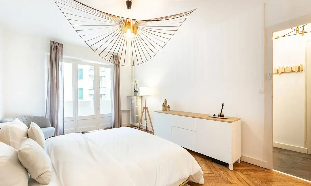 Éclairage chambre : suspension design en bois, lampe sur trépied et commode blanche dans une chambre moderne.