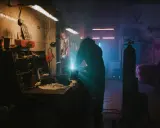 Un soudeur travaille dans un garage sombre, éclairé par des néons. La question "dans quel sens installer un néon dans un garage" plane dans l'air.