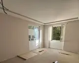 Chambre en cours de rénovation avec un faux plafond élégant, deux fenêtres ouvertes sur la verdure et des matériaux de construction au sol.