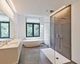 Salle de bain moderne avec baignoire îlot, double vasque et douche à l'italienne. L'éclairage intégré en hauteur applique une ambiance douce.