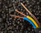 Trois fils électriques aux conducteurs en cuivre, dont un fil marron électrique, sortent d'un câble noir sur un fond de granulés noirs.