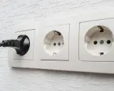 Une prise C16 noire est branchée dans une prise murale blanche. Deux autres prises sont visibles.