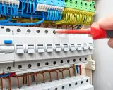 Main électrique avec disjoncteurs. Un tournevis rouge est utilisé pour ajuster une connexion, aidant à comprendre comment savoir quel fusible changer.