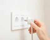 Main d'une personne branchant une prise électrique dans une prise murale triple.