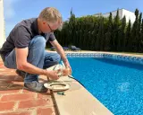 Homme près d'une piscine, tenant une pièce de la pompe. Il vérifie le disjoncteur pompe piscine pour s'assurer que tout fonctionne.