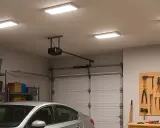 Quel éclairage pour un garage ! Quatre panneaux lumineux éclairent un garage bien rangé avec une voiture, des étagères de rangement et un panneau d'outils.