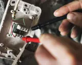 Mains électriques sous tension, un technicien vérifie un fusible qui chauffe avec un multimètre.