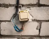 Interrupteur électrique beige en saillie sur un mur de briques, fils dénudés bleus et blancs.