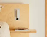 Applique murale au design épuré, à la bonne hauteur pour une tête de lit en bois clair. Lunettes posées sur un livre.