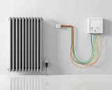 Radiateur électrique argenté relié par des câbles colorés à une prise murale. L'alimentation du radiateur électrique est assurée par ce système.