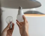 Une ampoule sans électricité, une ampoule LED moderne et une main tenant les deux, prête à remplacer l'ancienne.