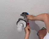 Un homme installe un luminaire au plafond avec un tournevis.