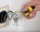 Mainteneur ajustant un fil bleu et marron dans une prise électrique.