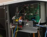 Vue rapprochée des composants internes d'une pompe à chaleur, incluant la carte électronique et le disjoncteur.