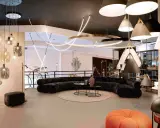 Un salon moderne avec un canapé incurvé noir, des tables basses, un tapis rond et une variété d'ampoules design suspendues au plafond.