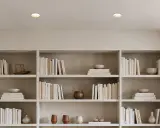 Éclairage discret d'un faux plafond avec spots encastrés, illuminant des étagères remplies de livres et d'objets décoratifs.