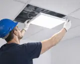 Un ouvrier installe une dalle LED design dans un faux plafond.