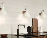 Trois appliques murales blanches avec un bras noir et une base dorée, éclairant un mur de carreaux blancs. Le branchement applique murale avec interrupteur est discret.