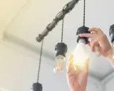 Main d'une personne installant une ampoule gradable dans un lustre.