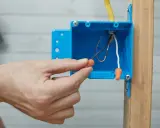 Main tenant utilise un connecteur pour condamner une prise électrique. Les fils électriques sont visibles dans la boîte bleue.