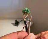 Connexion de fils électriques colorés à un connecteur vert. Un petit point lumineux attire l'œil sur le fil blanc.