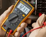 Un électricien utilise un multimètre pour mesurer la tension. Il cherche à comment reconnaître la phase du neutre en testant les fils d'un panneau électrique.
