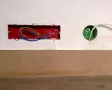 Boîtier rouge avec fils électriques colorés, prêt pour un interrupteur compteur électrique. Une boîte verte avec un câble blanc est visible à droite.