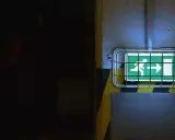 Panneau de sortie de secours vert lumineux, indiquant la direction à suivre. Le **baes signification** est claire : sécurité et évacuation.