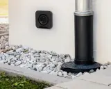 Une prise femelle étanche noire est fixée au mur blanc, à côté d'une descente d'eau.